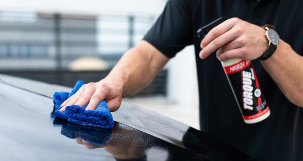 Hands cleaning car with microfiber cloth and spray cleaner for a shiny finish.